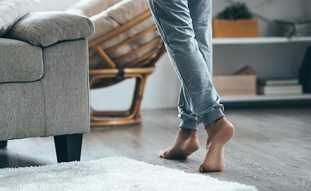 Bare feet running across a floor in a room with a sofa. A white carpet lies in front of the sofa. 